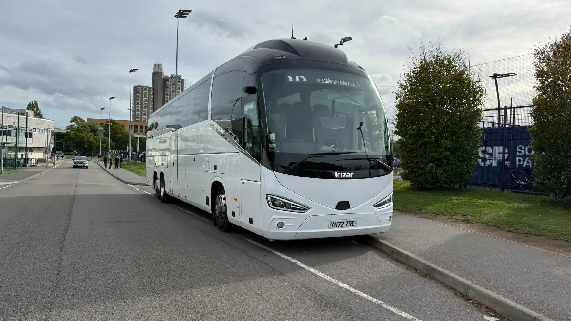 White coach parked beside a sports ground before a university fixture