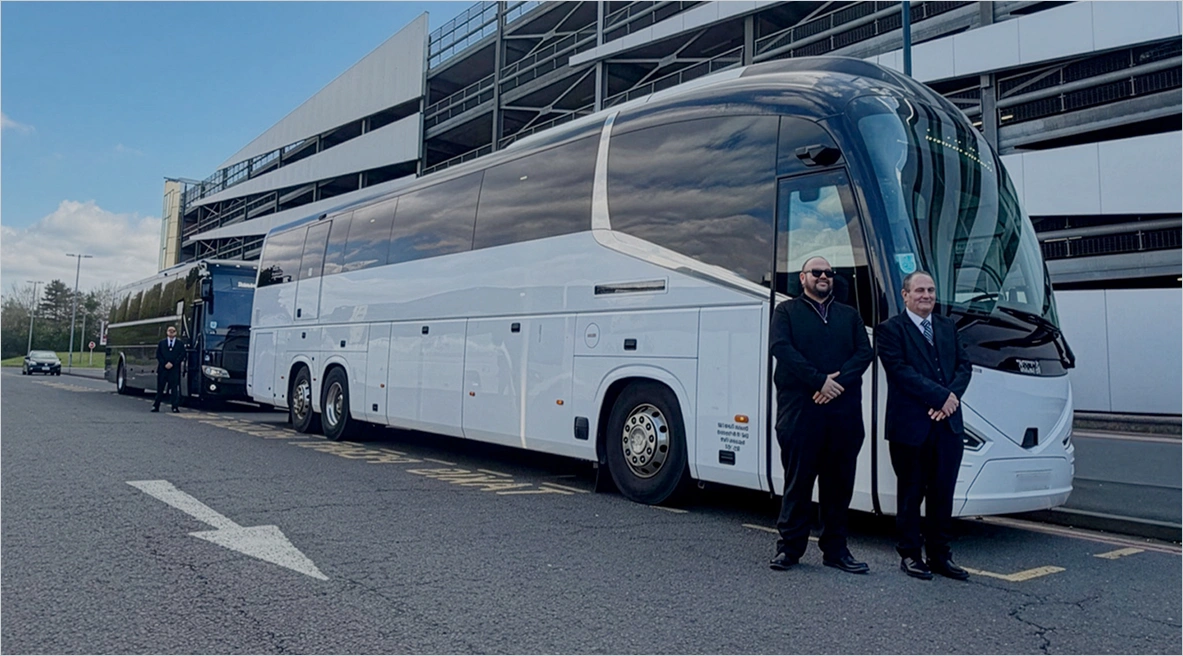 Luxury UK coach hire service with modern white executive coach parked outside airport terminal, professional drivers standing beside vehicle