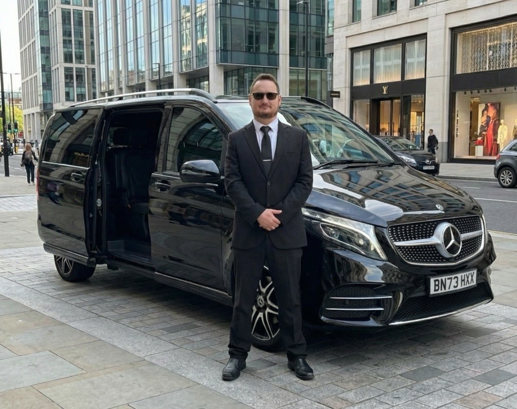 Premium chauffeur-driven Mercedes V-Class for private hire in the UK, suited driver standing beside luxury black MPV in city street